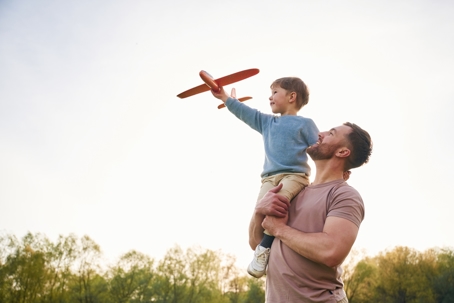 Dad carries his son on his shoulders while the boy holds a toy plane—symbolizing stable parenting time under a Florida temporary order during a pending case.